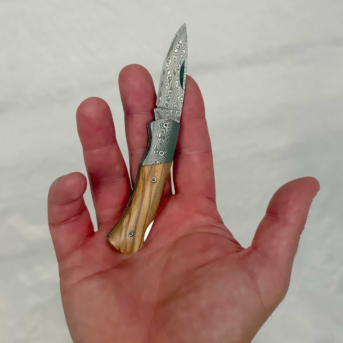 Magnum Damascus Mistress – elegantes Damast-Taschenmesser mit Olivenholzgriff. Größenvergleich des Taschenmessers in der Hand.